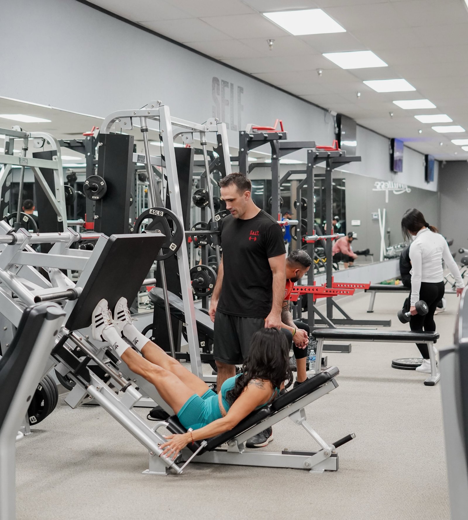 Trainer coaching a member on the leg press